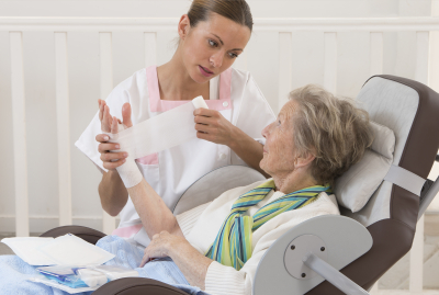 Nurse taking care of senior woman in retirement home bandaging her arm